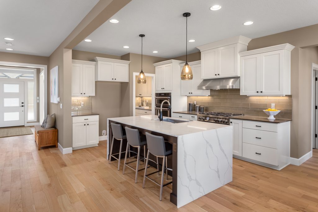 White quartz waterfall island in a modern Mid-Michigan kitchen with warm hardwood floors and white cabinetry.