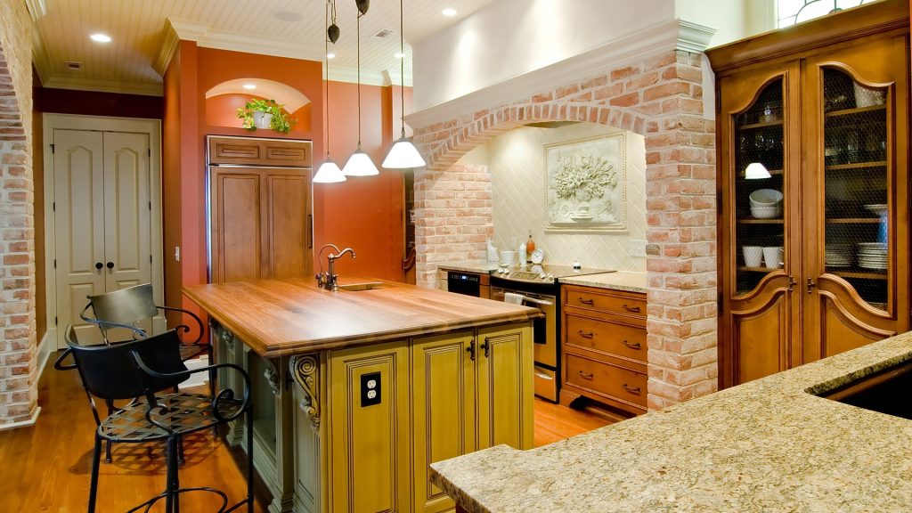 Wood butcher block kitchen island with a stone perimeter countertop and undermount sink along the back wall