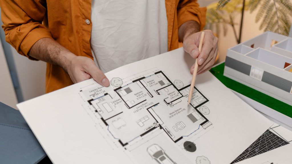 A homeowner and a kitchen designer comparing a printed kitchen floor plan against measurements at a showroom table