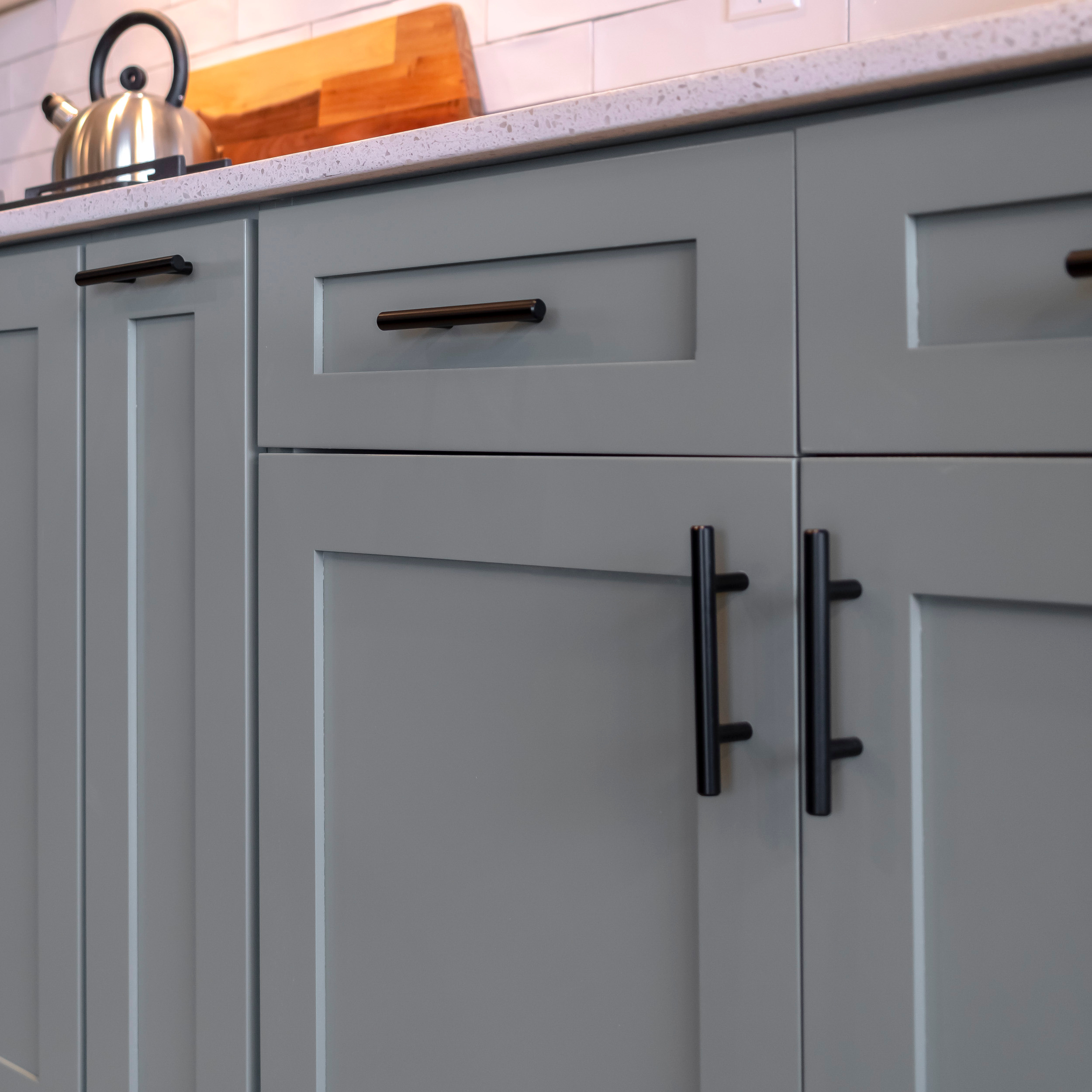 Grey shaker kitchen cabinets with a black bar pull on the drawer front and vertical black T-bar pulls on the base cabinet doors