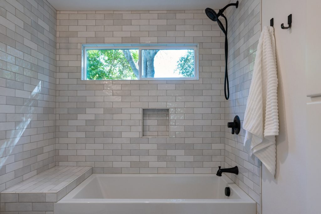 Square tiled shower niche recessed into a white subway tile wall above an alcove tub, with the shower valve on the adjacent wall