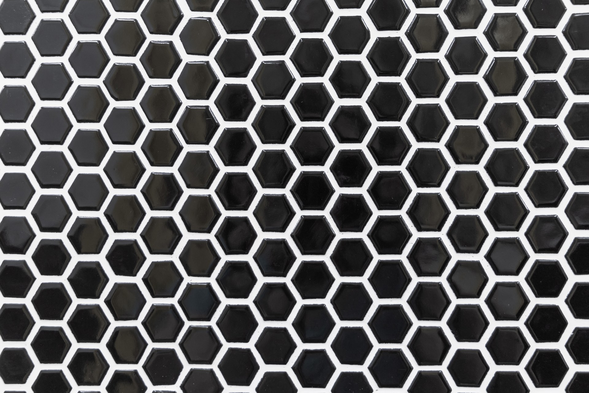 Glazed black hexagon mosaic tile set with bright white grout, where the contrasting joints outline every individual tile