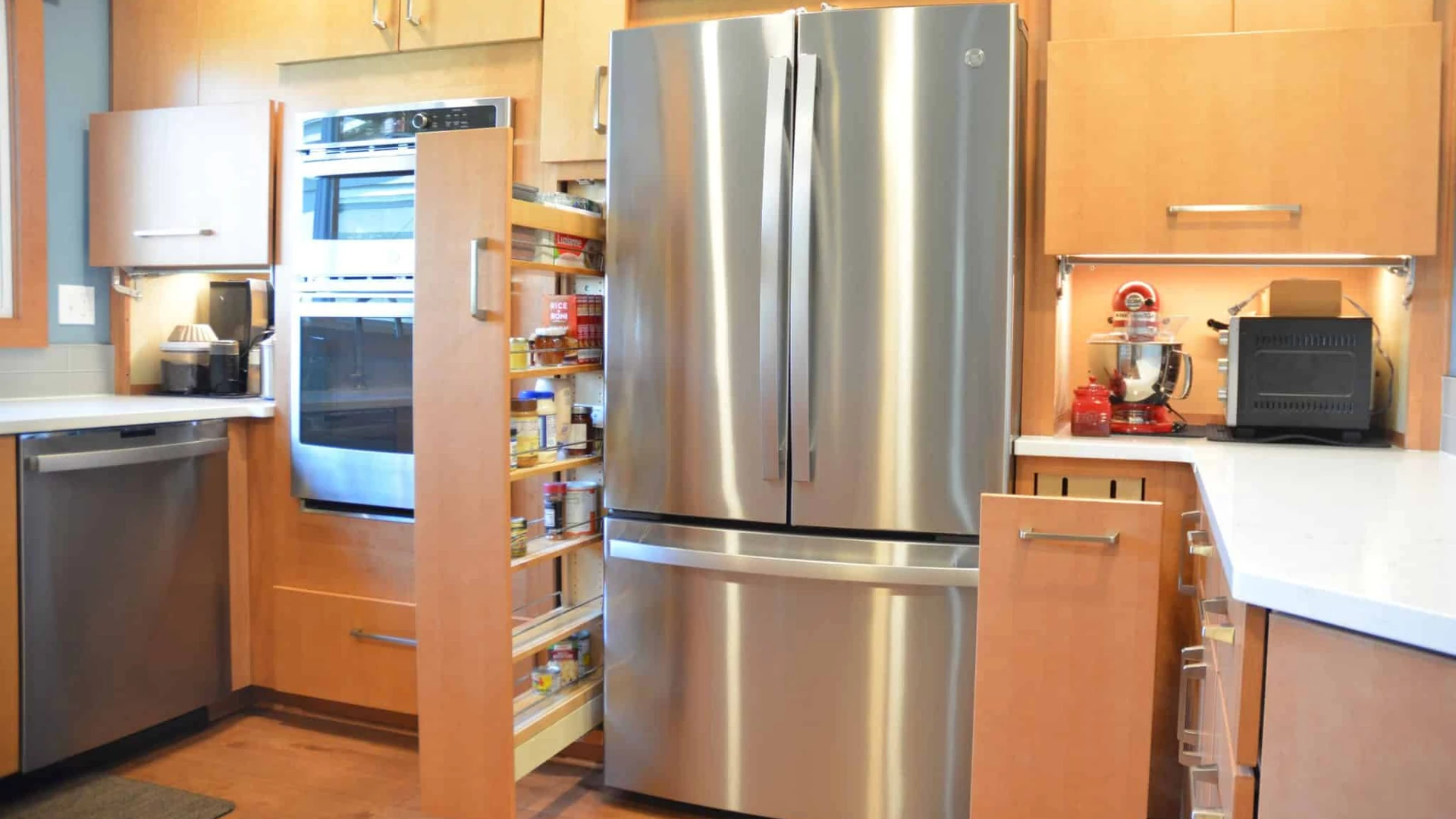 Kitchen with flat-panel wood cabinets, an open pull-out spice cabinet and an open pull-out base cabinet beside a stainless refrigerator and wall ovens