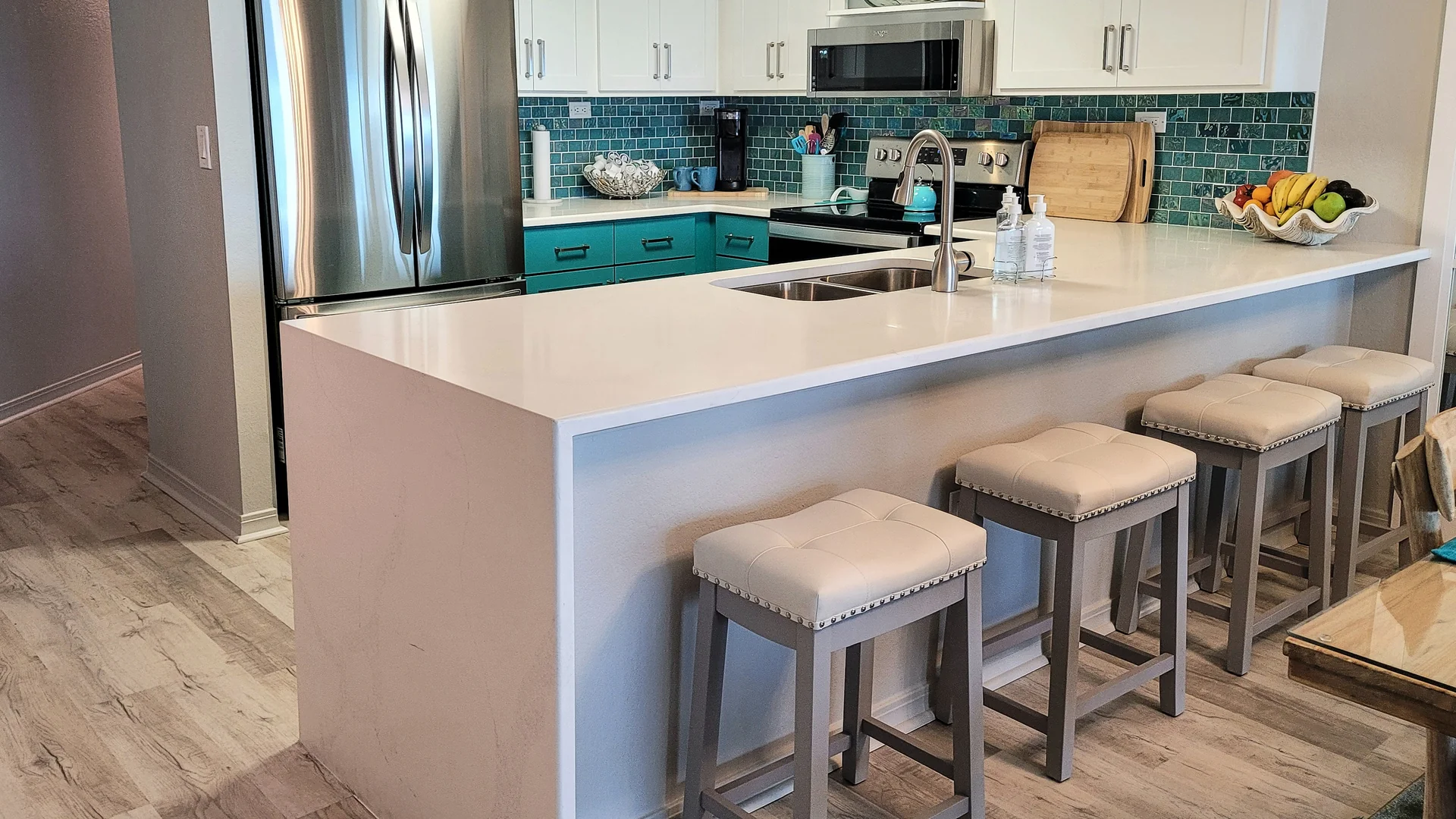 Four upholstered counter-height stools lined up along a white waterfall kitchen peninsula with a sink