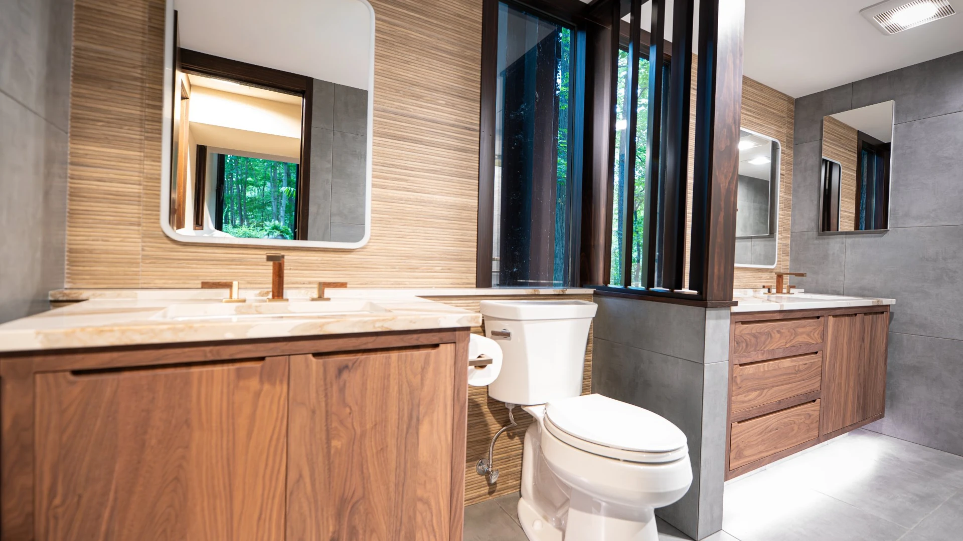 Modern bathroom with wood-grain vanities, veined countertops, textured wall tile and large gray floor tiles