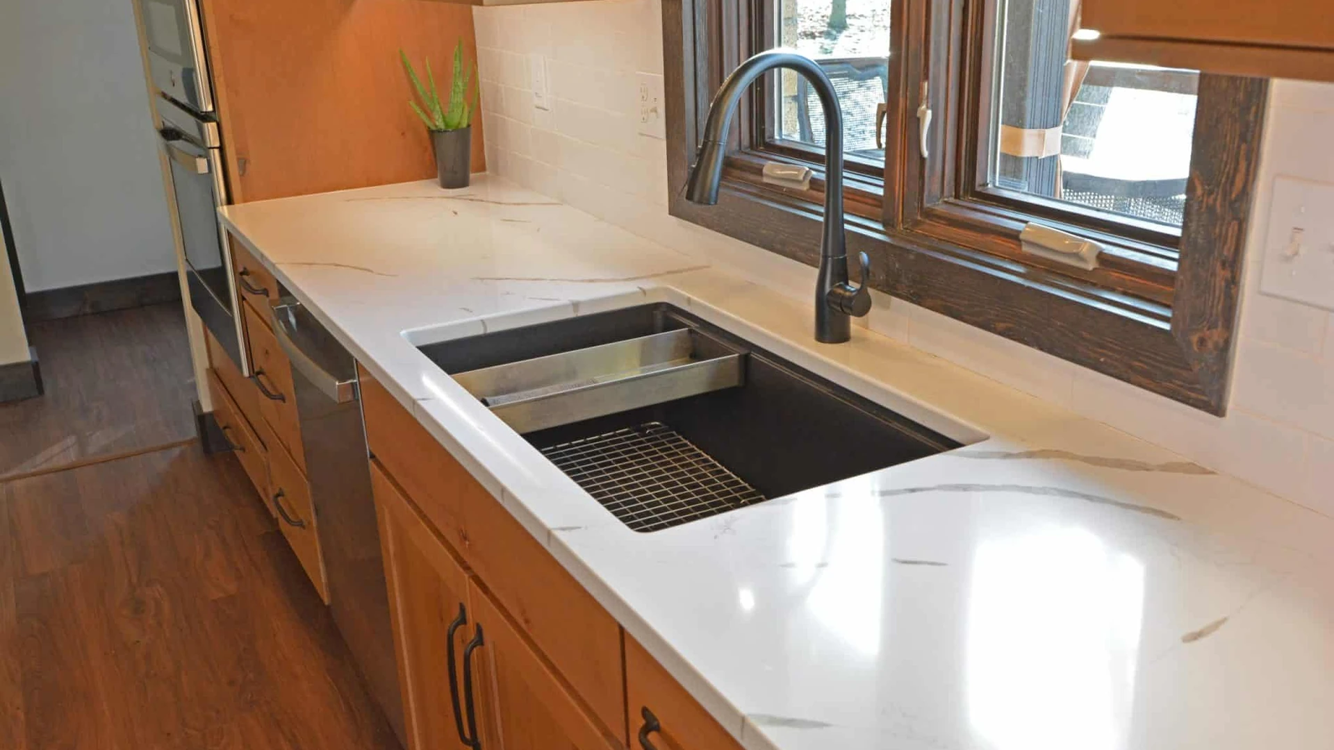 Dark kitchen sink with a pull-down faucet set in a white veined countertop above wood-tone base cabinets, beside a dishwasher