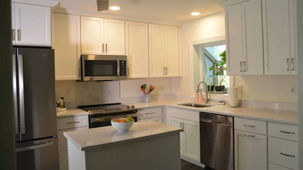 White kitchen cabinets with a stainless dishwasher next to a sink under a window, and a gray island in front of the range