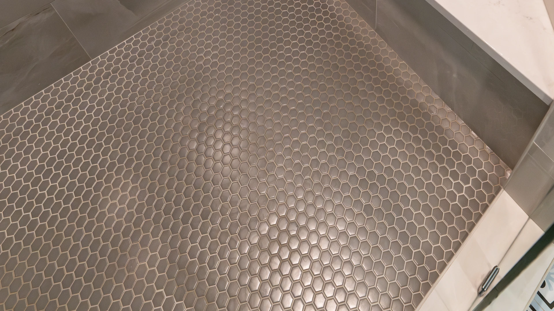 Gray hexagonal mosaic tile covering a tiled shower floor beside a bench with a white top