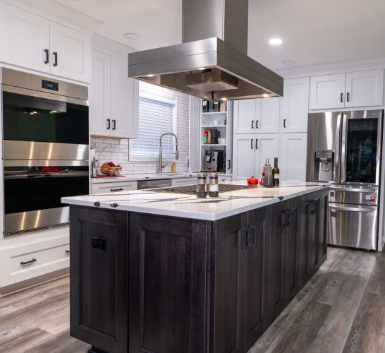 White kitchen with a dark island, island cooktop and large suspended metal hood.