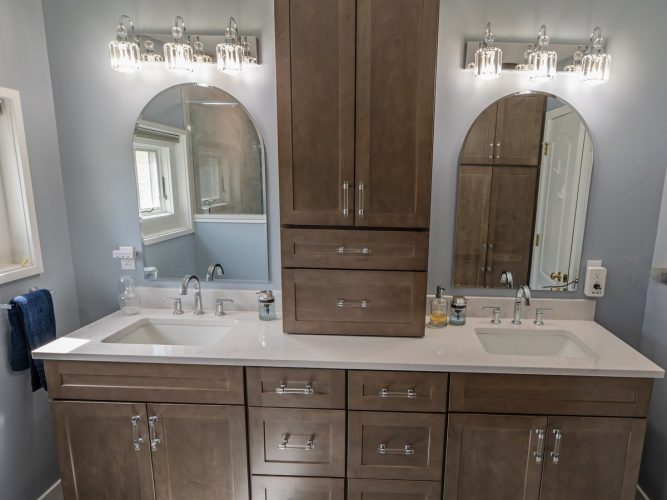 Wood-grain double vanity with a tall central storage cabinet between two arched mirrors