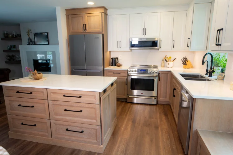 Kitchen with white upper cabinets, light wood-grain base cabinets and a drawer island with a pale countertop