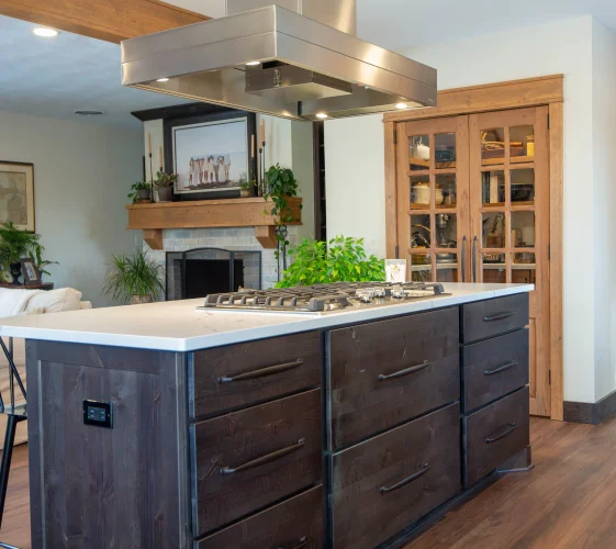 Dark wood-grain kitchen island with a cooktop beneath a broad suspended metal hood
